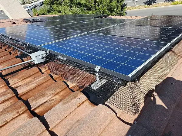 Black critter guard mesh installed along the tile roofline under the edge of a solar array.